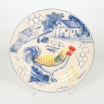 FAIANÇA, um (1) medalhão decorativo pintado a mão representando paisagem rural com galinha e pintinhos, policromado com predominância da tonalidade azul, marca LUIZ SALVADOR (destacado mestre da arte de pintura em faiança na olaria de Alcobaça em Portugal, veio para o Brasil e fundou no ano de 1950 uma fábrica em Itaipava, região serrana do Rio de Janeiro, ainda em atividade), medindo 27,5 cm diâmetro, vide foto.
