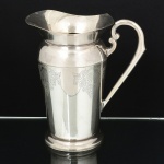 METAL PRATEADO, uma (1) jarra refresqueira com ornamentação em baixo relevo em volutas e elementos vegetalistas, possui retentor de gelo, alças curvilíneas com terminações em volutas, marca EBERLE (Abramo Eberle 1880, Monte Magrè 1945, Caxias do Sul, veio com uma das primeiras levas de imigrantes italianos para o Brasil em 1884 junto com seus pais Giuzeppe Eberle e Luigia Zanrosso, seu pai abriu uma pequena funilaria mas como tinha que trabalhar na lavoura quem cuidava era a mãe e o pequeno Abramo ajudava na funilaria; em 1896 quando o pai resolveu vender a funilaria para concentrar os esforços da família na lavoura Abramo, com 16 anos de idade, se propôs a comprá-la do pai, em 1918 já com o nome Abramo Eberle & Cia iniciou a fabricação de talheres e utensílios de mesa, morreu em 1945 com 65 anos de idade e os filhos deram continuidade aos negócios até 1984 quando venderam para o Grupo Zivi), medindo 22 cm altura, sinais de uso, mossa na base, vide foto.
