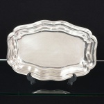 METAL PRATEADO, uma (1) travessa quase oval de borda alta, ondulada e plissada, sem marca de manufatura aparente, medindo 29,5 x 20 x 3 cm, sinais de uso, vide foto.