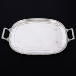 METAL PRATEADO, uma (1) bandeja quase retangular com borda ovalada, ornamentação relevada no padrão Império Napoleônico com frisos intercalados por X, alças na mesma padronização com detalhes em folhas, marca FRACALANZA (tradição desde 1884), medindo 42,5 x 33 cm mais as alças, sinais de uso, vide foto.