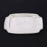 AÇO INOX, uma (1) travessa, quase retangular com quinas chanfradas, ornamentação no padrão Império Napoleônico com frisos intercalados por X, sem marca de manufatura aparente, medindo 38 x 23,5 cm, sinais de uso, vide foto.