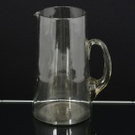 VIDRO, uma (1) jarra refresqueira, formato ligeiramente cônico, alça curvilínea e canelada, incolor e translúcida com leve toque fume, medindo 23 cm altura, sinais de uso, vide foto.