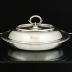 METAL PRATEADO, uma (1) travessa oval com tampa, adaptável para duas travessas, marca FRACALANZA (tradição desde 1884), ornamentação relevada no padrão Império Napoleônico com frisos intercalados por X, medindo 27 x 20,5 cm, sinais de uso, vide foto.