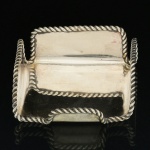 METAL PRATEADO, um (1) porta cartão com borda relevada em corda, sinais de que falta parte, sem marca de manufatura aparente, medindo 7,5 x 7,5 x 2,5 cm, sinais de uso, vide foto.