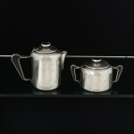 AÇO INOX, dois (2) itens cilíndricos com detalhes em polímero na tonalidade preta: 1 cremeira e 1 açucareiro, marca WOLFF (tradição desde 1894), lisos, medindo a maior peça 10,5 cm altura, ambos com sinais de uso, vide foto.