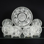 CRISTAL, conjunto para sobremesa com sete (7) itens: 1 travessa circular de borda alta, grossa incolor e translúcida, lapidada em sulcos, estrelas e rosáceas, medindo 28,5 cm diâmetro e 3,5 cm altura; 6 taças na mesma padronização, medindo 14,5 cm diâmetro e 3 cm altura, sinais de uso, vide foto.