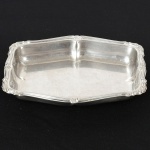 AÇO INOX, uma (1) travessa de borda alta, quase retangular, borda relevada em frisos e volutas na técnica mecanizada de estamparia, medindo 25 x 18 cm, sinais de uso, vide foto.