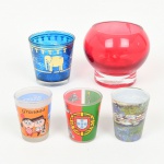 VIDRO, cinco (5) itens: 1 vaso quase esférico com base cilíndrica, incolor e translúcido com esmaltação interna na tonalidade cereja, medindo 10,5 cm diâmetro e 9 cm altura; 1 copo, ligeiramente obcônico, incolor e translúcido, parte interna com esmaltação na tonalidade azul e externa com elefantes dourados, ambas com falhas, medindo 7,5 cm de altura e diâmetro; 3 copinhos, incolores e translúcidos, ornados com faixas em decalque e distintas, policromadas, souvenires de lugares variados, dois deles com detalhes acetinados, medindo 6 cm altura, todos os itens com sinais de uso, vide foto.