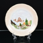 PORCELANA, um (1) prato decorativo ornado com paisagem lacustre, pintado a mão, atelier YONE, borda comarremates a ouro, marca SCHMIDT (Pomerode, SC; Mauá, SP; Campo Largo, PR, fundada em 1945, ainda ematividade, maior fábrica de porcelana da América Latina), medindo 25,5 cm diâmetro, vide foto.
