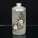 VIDRO, um (1) vaso cilíndrico, incolor e translúcido, corpo acetinado, esmaltação pintada a mão com flores empolicromia, tampa adaptada em alumínio, medindo 16,5 cm altura, sinais de uso, vide foto.