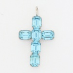 BIJUTERIA, uma (1) cruz confeccionada em metal prateado com strass na tonalidade azul, medindo 3,5 cm, videfoto.