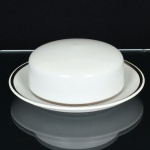 PORCELANA, uma (1) manteigueira com presentoir acoplado, clássica, tonalidade branca, arremates com frisosprateados, linha MEDAILLON, manufatura RENNER (Porto Alegre, RS, fundada em 1942; em 1998 foi vendida para aVista Alegre de Portugal; em 1999 mudou a razão social para Vista Alegre do Brasil), medindo 17 cm diâmetro, videfoto.