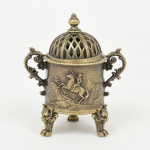 BRONZE, um (1) incensório no formato de vaso, ornamentação relevada representando paisagem com Napoleão acavalo, alças curvilíneas relevadas em flores e volutas, tampa vazada encimada por pinha, pés no formato de cabeças detigre com terminações em garra, medindo aproximadamente 6,5 cm altura, vide foto.