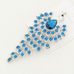 BIJUTERIA, um (1) imponente broche representando pavão, confeccionado em metal prateado com apliques emzircônios azuis e incolores, medindo aproximadamente 10,5 x 5 cm, vide foto.