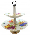 Fruteira dupla em porcelana adornada com coloridos motivos frutais, vegetalistas e filetes dourados; pratos com bordas onduladas; haste central interna em metal. Medidas: 32 x 27 cm.