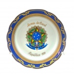PORCELANA SCHMIDT, BRASIL - Prato decorativo adornado na borda com volutas em dourado e faixa em legítimo azul cobalto, e em sua galeria central com o Brasão da República dos Estados Unidos do Brasil. Medidas: 25 cm (diâm.).