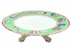 Antigo centro de mesa circular com borda decorada com colorida inscrição em alemão sobre faixa na cor verde; base com seis pés curvos em forma de volutas. Em cerâmica esmaltada. Marca de manufatura não identificada. Medidas: 32 x 7 cm. Com bicados, fios de cabelo e bicados em alguns pontos. Pintura desvanecida em alguns pontos.