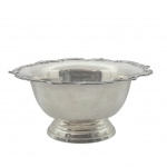 Grande bowl em metal espessurado à prata, decorado na borda com volutas e motivos vegetalistas em relevo; base pedestal com detalhes escalonados. Medidas: 43 cm (diâm.) x 20 cm.