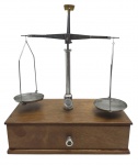 BALANÇA DE PRECISÃO - Antiga balança de precisão, com base em madeira, estilo pequena móvel. Balança em metal, com estojo em madeira tendo pesos e uma pinça. Na base possui uma gaveta para guardar os pesos com o estojo e outras coisas. Medida: 29cm x 35cm. Observação: Não aferida, necessita manutenção, parte interna da gaveta com pequena avaria, ausência de 2 pesos. Possui pequenas marcas.