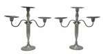 Par de candelabros em estanho de acabamento escovado, com três nichos para velas em formato de disco, sendo dois ligados à haste central através de braços em S, no formato de volutas; haste central com detalhes boleados. Medidas: 34 x 35 cm.