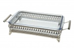 Porta-refratário retangular em metal espessurado à prata, com refratário de vidro da marca Marinex, com alças laterais e corpo com detalhes vazados; base com quatro pés gravados com motivos florais e volutas. Medidas: 44 x 22 x 9 cm. Com desgastes no banho.