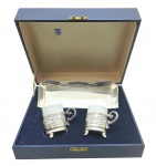EBERLE / SCHMIDT- Estojo composto por 02 xícaras de café em porcelana da manufatura Schmidt com suporte e uma bandeja em metal espessurado à prata, da empresa Eberle. Suportes das xícaras com detalhes florais e vegetalistas vazados, alça em forma de volutas e base trípode. Medidas: 28 x 24 x 10 cm. Alça do estojo com avaria
