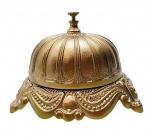 Rara e antiga campainha de mesa de recepção, em bronze, final do séc. XIX - início séc. XX e de inspiração rococó. Acionador em forma de disco e cúpula e com detalhes canelados; base trípode ampla e larga, recortada com volutas em relevo. Medidas: 19 x 14 cm. Recebeu acabamento em textura metálica dourada.