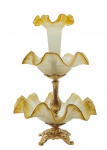 Centro de mesa clássico composto por três elementos, um central e alongado, e dois circulares, com bordas onduladas semelhantes a babados, em vidro ocre fosco. Estruturado em bronze cinzelado com padrões fitomórficos; base quadripartida adornada com volutas. Medidas: 49 x 33 cm. Bronze recebeu acabamento em textura metálica dourada.