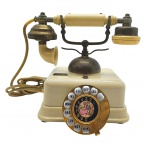 Antigo telefone de mesa, de estilo retrô, em metal e baquelite; disco rotativo em algarismos indo-arábicos, em letras do alfabeto, e com colorida ilustração de cena galante no centro; fabricação japonesa. Medidas: 24 x 17 x 13 cm. Não testado. Metal dourado escurecido devido à passagem do tempo; pintura com ínfimos desgastes.