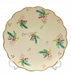 WEISS - Prato decorativo com borda ondulada adornada com filete dourado e coloridos padrões florais e vegetalistas em dourado. Em cerâmica esmaltada bege, pintada à mão. Medidas: 30 cm (diâm.). Com bicados e sinal de restauro na borda.