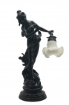 Luminária de mesa figurativa, de inspiração Art Nouveau, com a representação de figura feminina em trajes esvoaçantes, apoiada sobre base circular escalonada; cúpula em vidro opalinado moldado no formato de tulipa, com bordas transparentes; decoração complementada por elementos naturalistas em relevo; estruturada em metal com acabamento em textura na cor preta. Medidas: 67 x 37 x 23 cm. Não testada.
