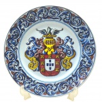 OUTEIRO AGUEDA PORTUGAL - OURIVESARIA XAVIER LISBÔA - Antigo medalhão em colorida cerâmica esmaltada portuguesa, decorada com motivos fitomórficos e um brasão em sua área central. Numerada. Com assinatura da artista (Breda). Medidas: 38 cm. Com ínfimos bicados e manchados devido à passagem do tempo.