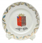 Medalhão decorado à mão com padrões fitomórficos na borda e o brasão do Barão de Ivinhema em sua galeria central. Assinatura do artista e data no verso. Em porcelana colorida com detalhes em dourado. Medidas: 30 cm (diâm.).