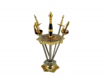 METAL DOURADO, quatro (4) espetos de petiscos de Toledo, em metal dourado e prateado, com formato de pequenas espadas, acondicionados em suporte ornamentado, com base trabalhada, haste central torneada, medindo 10cm de altura. Apresenta sinais de oxidação.
