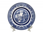 PORCELANA OXFORD, um (1) prato decorativo confeccionado em porcelana na tonalidade branca com decoração reproduzindo a cena dita POMBINHO WILLOW, borda ricamente em elementos geométricos na tonalidade azul, medindo 22cm de diâmetro.
