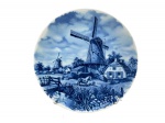 PORCELANA DELFT, um (1) prato decorativo confeccionado em porcelana na tonalidade branca, decorada por cena de fazenda holandesa com moinhos de vento na tonalidade azul, medindo 24cm de diâmetro.