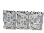 PORCELANAS, três (3) espelhos para interruptores confeccionados em porcelana na tonalidade branca, com pintura de flores e folhagens em policromia, com realces filetados e laçarotes em ouro, medindo 13x8,5cm, 1 bicado.