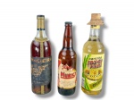 BEBIDAS, três (3) garrafas antigas/colecionáveis, sendo: A) uma garrafa de Macieira, bebida portuguesa, em vidro transparente com líquido aparente, rótulo escuro bastante desgastado e tampa dourada; B) uma garrafa menor Murici, aguardente composta, com rótulo em tons creme, vermelho e amarelo, tampa metálica; C) uma garrafa de Caninha Chapéu de Palha Ouro, conteúdo 1000ml, com rótulo colorido decorado com palha e cana, tampa com acabamento em palha trançada, todas garrafas lacradas, porém, sem garantia de integridade do líquido.