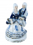 ESCULTURA, um (1) grupo escultórico representando casal de fidalgos com caixa musical, confeccionada em porcelana na tonalidade branca com realces e elementos florais na tonalidade azul e filetes em ouro, caixa musical não funciona, medindo 18,5cm de altura.