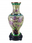 CLOISONNÉ, um (1) vaso confeccionado em cloisonné com rica decoração floral e vegetalista sobre fundo amarelo com realçes em douração, apoiada sobre peanha em madeira, medindo 23,5cm de altura. Apresenta falha na borda.