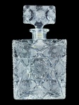 CRISTAL, uma (1) garrafa para whisky confeccionada em cristal translucido, ricamente lapidada por pingos de diamante, estrelas, caneluras e palmas em baixo relevo com fundo estrelado, tampa com colado, apresenta bicado na base, medindo 25x14x6,5cm.