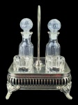 VIDRO e METAL PRATEADO, conjunto com licor com quatro (4) peças confeccionadas em vidro translucido com moldagem de caneluras, sendo: A) 2 licoreiras, medindo 14,5cm de altura e B) 2 copos para licor, medindo 4,5x4,5cm, acondicionados em suporte adaptado em metal prateado, medindo 20x15x15cm.