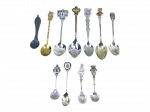 COLECIONISMO, onze (11) colheres de souvenir/coleção em metal, sendo peças em metal prateado, dourado e uma escurecida, com cabos trabalhados, brasões, escudos, inscrições e motivos regionais diversos. Inclui exemplares com bojos lisos e em formato de concha, além de peças com decoração em relevo e esmaltação colorida.