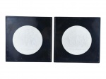 QUADROS, duas (2) placas redondas confeccionadas em biscuit na tonalidade branca, decorado por cenas greco-romana em relevo, apoiada sobre placas quadradas em madeira laqueada na tonalidade preta com falhas na laqueação, medindo 22x22cm.