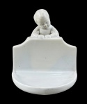 PORCELANA P II, um (1) saleiro confeccionado em porcelana na tonalidade branca decorado por Puttino em relevo, apresentando fio de cabelo na borda, medindo 11,5x11,5x10cm.