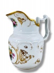 PORCELANA, uma (1) jarra confeccionada em porcelana na tonalidade branca, ricamente decorada por flores e folhagens em policromia, elementos vegetalistas em relevo na pasta, borda em recortes e alça vazada com filetes em ouro, medindo 20x18,5x11cm, apresenta restauro na borda.