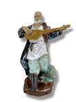 ESCULTURA ORIENTAL, uma (1) escultura confeccionada em cerâmica vitrificada com pintura esmaltada em policromia representando musicista, medindo 21,5cm de altura.