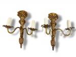 LUMINÁRIAS, par (2) de arandelas para duas lâmpadas no estilo neorrococó, confeccionadas em bronze com cinzselado de laçarotes, tochas e finalizado por pinha, hastes curvas com bobeche no feitio de flor, 1 vela da bobeche apresenta quebra e outro com ausência das duas velas, medindo 37,5x28,5cm.