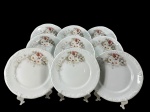 PORCELANA SCHMIDT, nove (9) pratos rasos confeccionadas em porcelana na tonalidade branca com pintura de elementos florais em policromia e filetes em prata, medindo 26cm diâmetro.