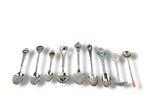 METAL PRATEADO, nove (9) pequenas colheres souvenir de coleção confeccionadas em metal prateado e uma peça em tom cobreado, com cabos ornamentados, alguns torcidos e trabalhados, terminais decorados com brasões, inscrições e aplicações esmaltadas coloridas, incluindo referências turísticas como Florida, Hawaii, Tobago e outras localidades.